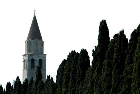 Foto del campanile di Aquileia, parzialmente coperto dalle chiome dei cipressi
